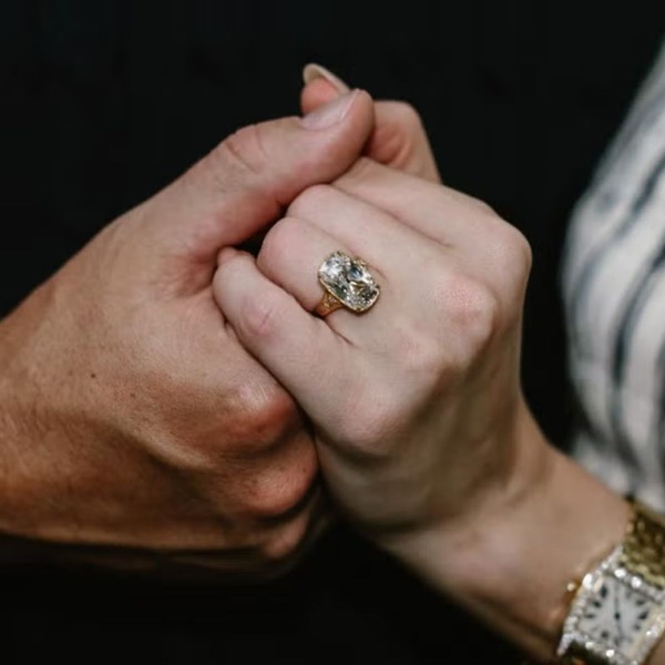 Two hands clasped, one adorned with a sparkling gemstone wedding ring, symbolizing a destination wedding.