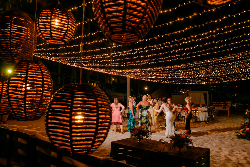 Guests dance barefoot on the sand beneath string lights and glowing Jordanian and Kievan lanterns, celebrating a magical destination wedding under the stars.