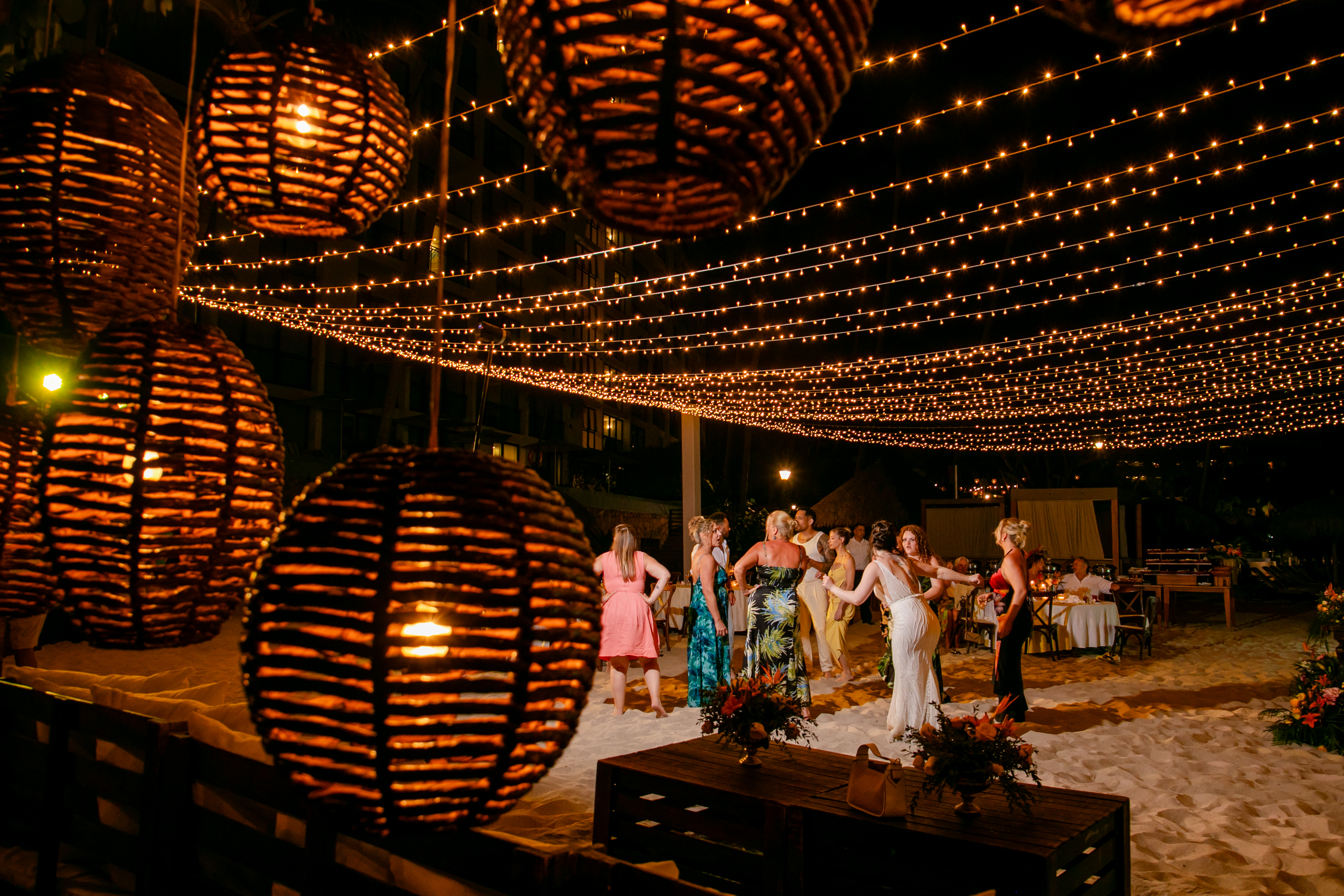 Guests dance barefoot on the sand beneath string lights and glowing Jordanian and Kievan lanterns, celebrating a magical destination wedding under the stars.