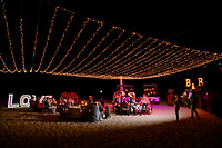 Nighttime destination wedding on the beach, with guests gathered under twinkling string lights and a large "LOVE" sign, celebrating Jordan and Kievan.