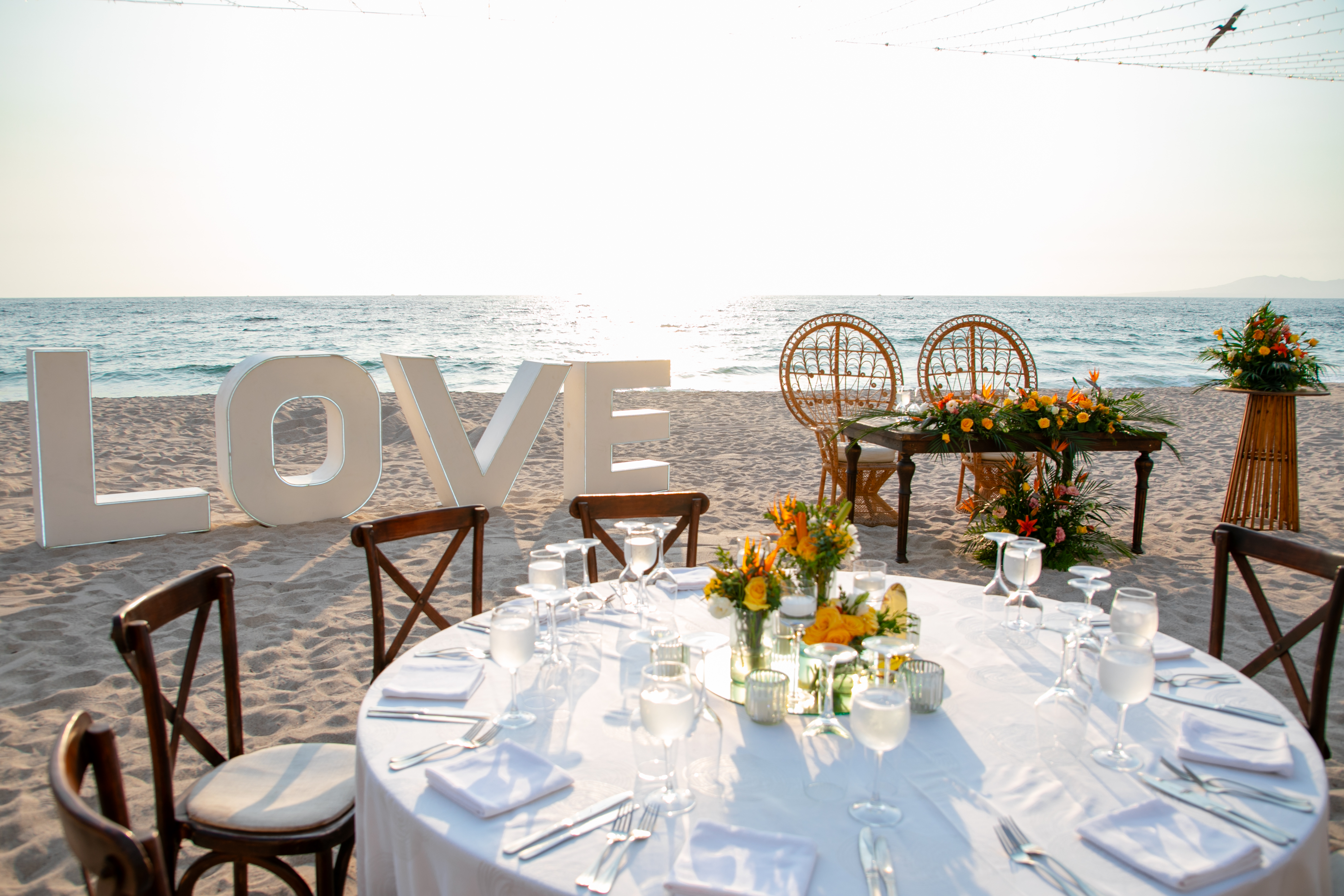 A stunning destination wedding setup by the sea, featuring a personalized "Jordan and Kievan" sign, an elegantly decorated table, and chairs arranged right on the beach.