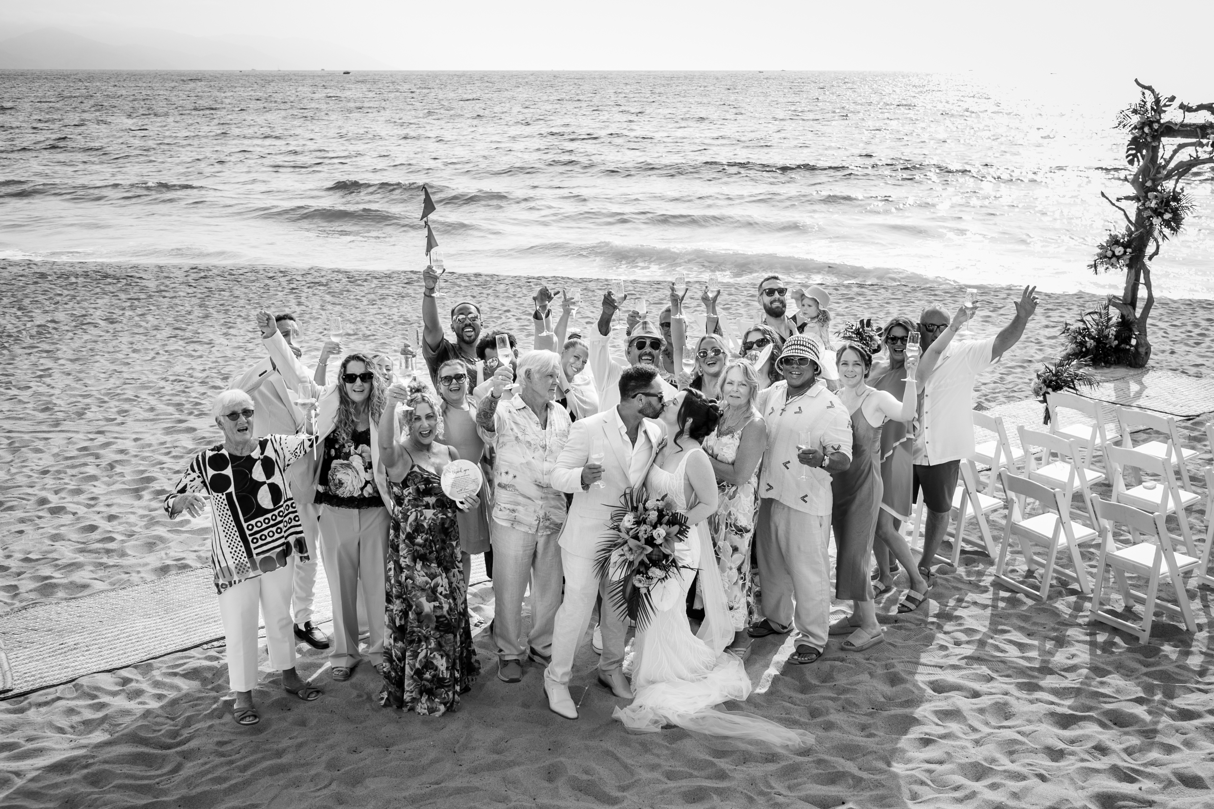 A destination wedding celebration unfolds on a sandy beach by the ocean, with the wedding party rejoicing by the shore.