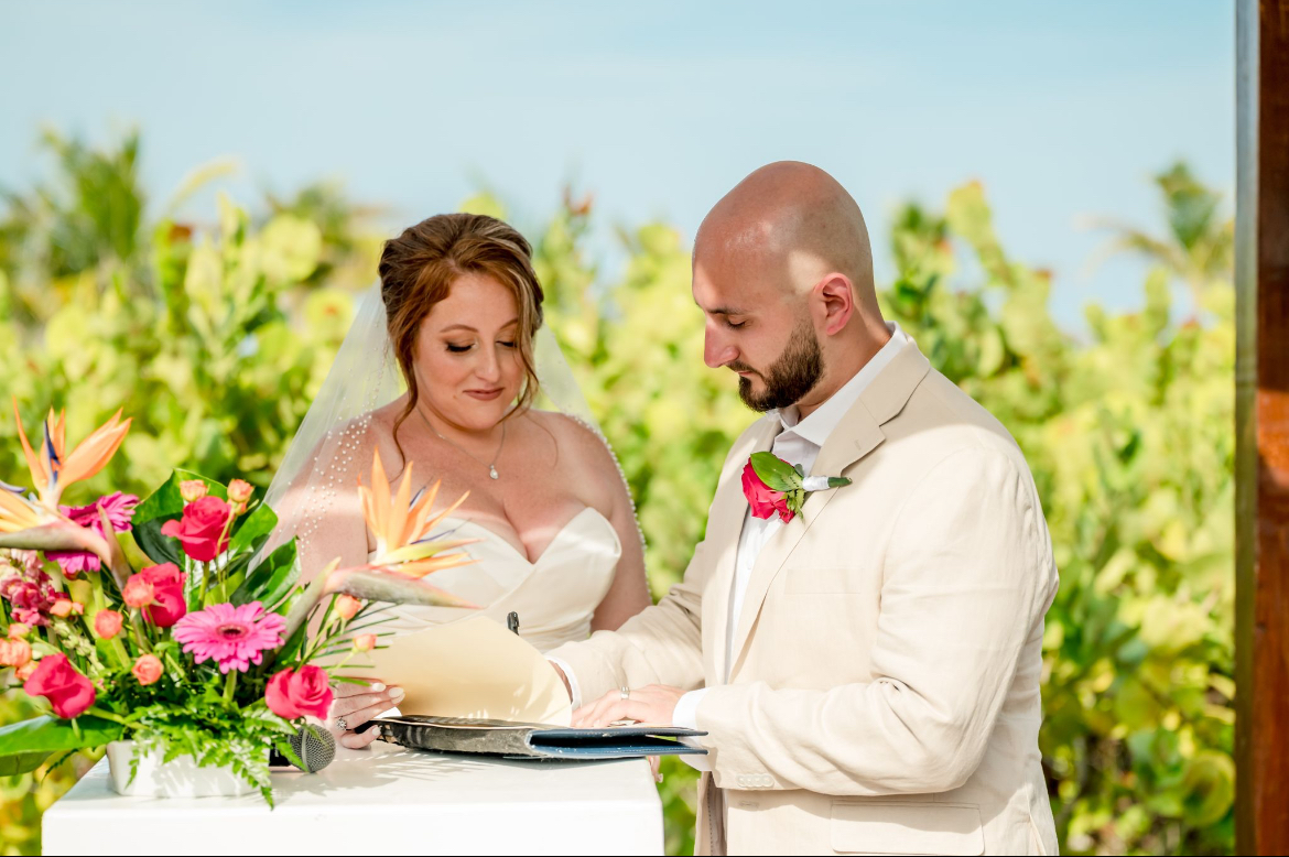 Mobolaji and Sylvia sign their wedding papers outdoors next to a flower arrangement at a destination wedding.