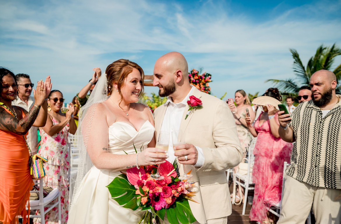 Mobolaji and Sylvia (Copy) smile with drinks at their destination wedding, surrounded by joyful guests outdoors.