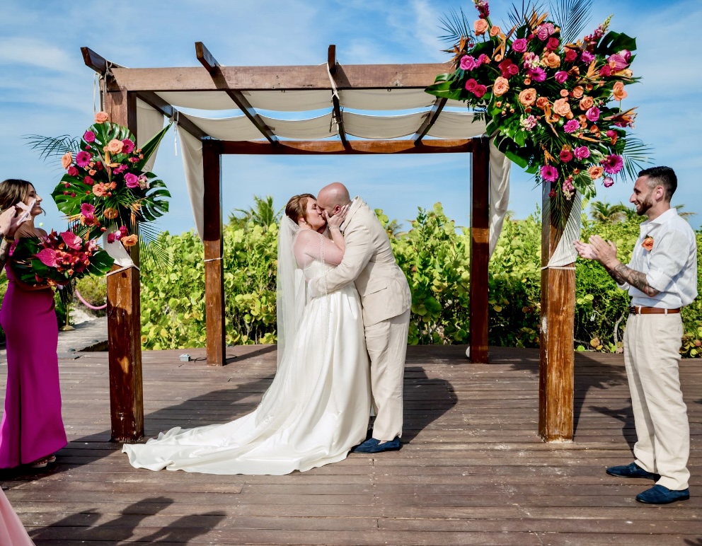 Mobolaji and Sylvia share a kiss beneath a pergola during their romantic destination wedding ceremony.