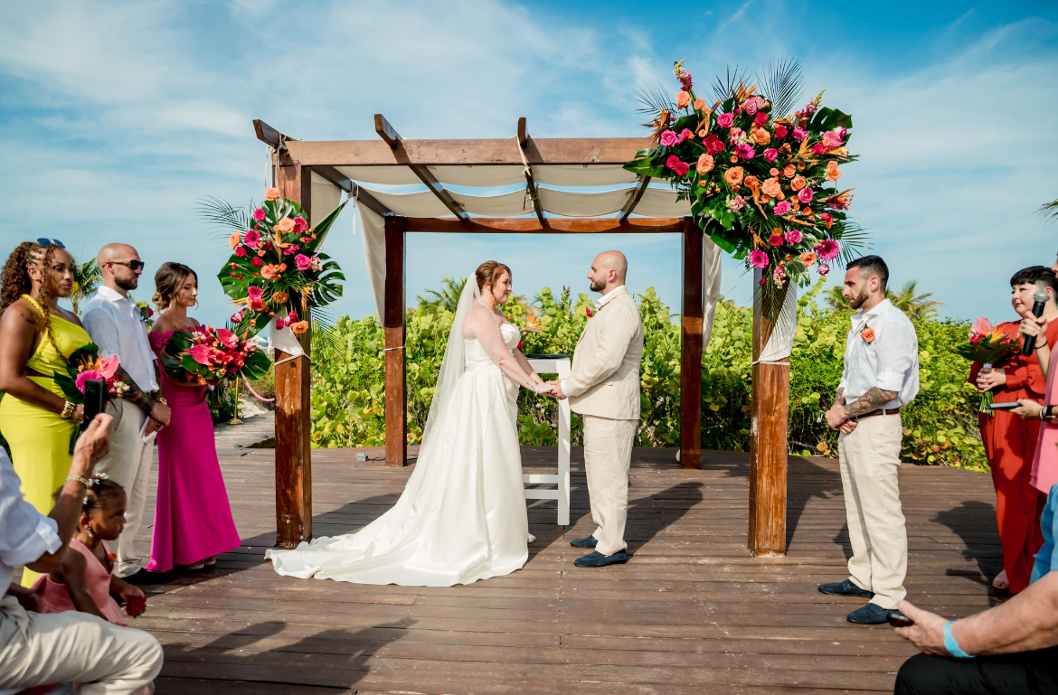 Mobolaji and Sylvia exchange vows at their destination wedding altar with attendants on a sunny day.