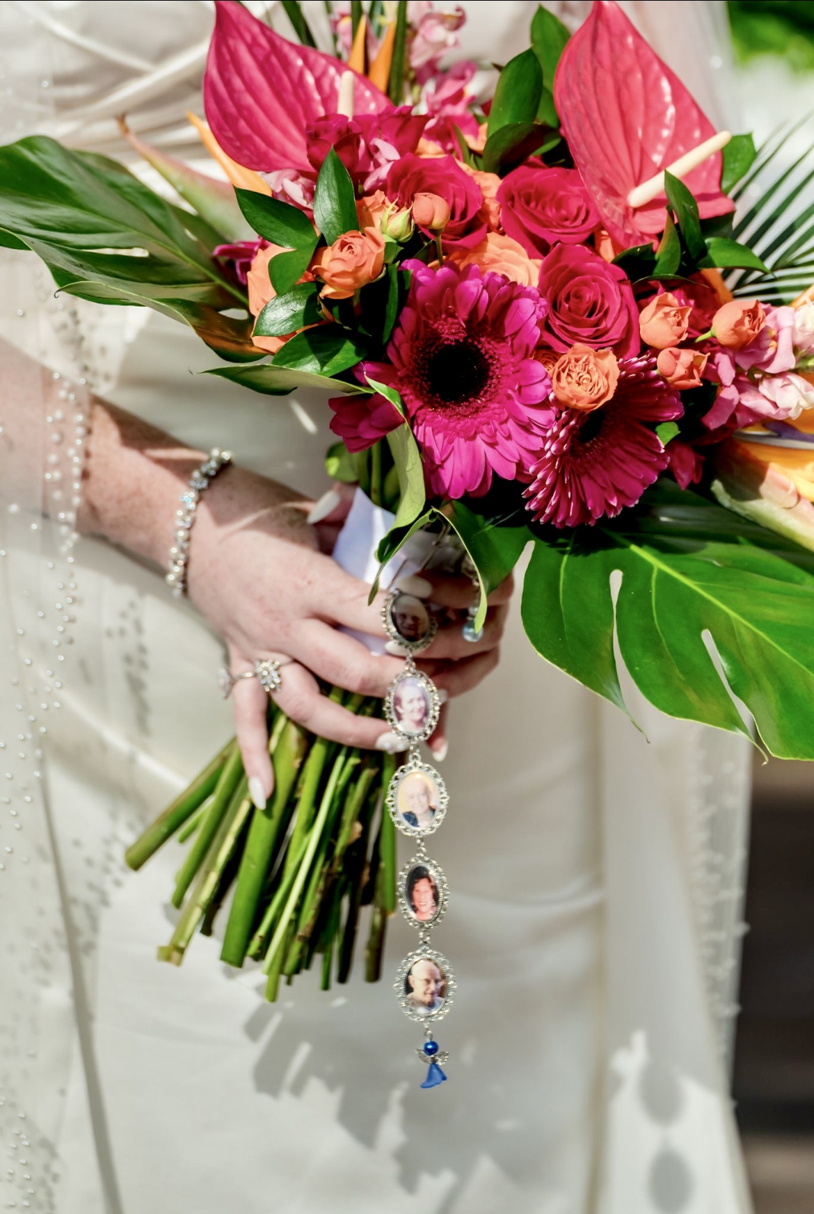 Bride at a destination wedding holds the Mobolaji and Sylvia bouquet with pink, orange blooms and photo charms.