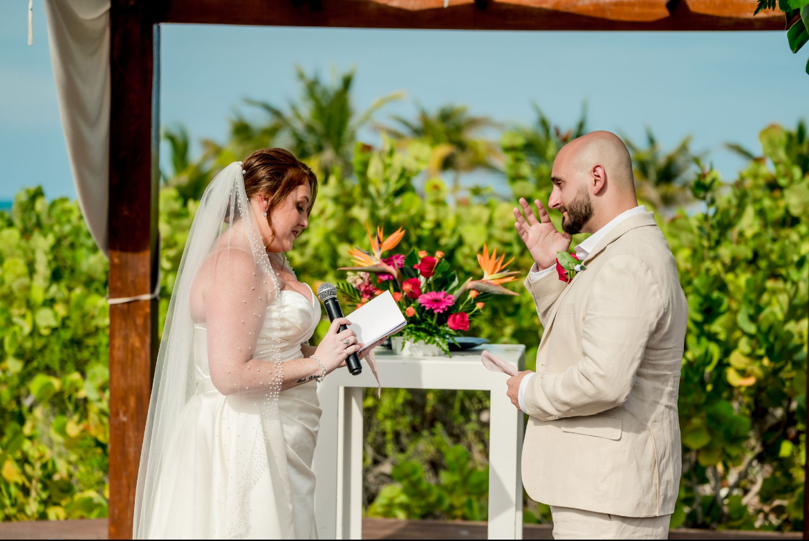 At their destination wedding, Mobolaji and Sylvia exchange vows outdoors by a flower-adorned table.