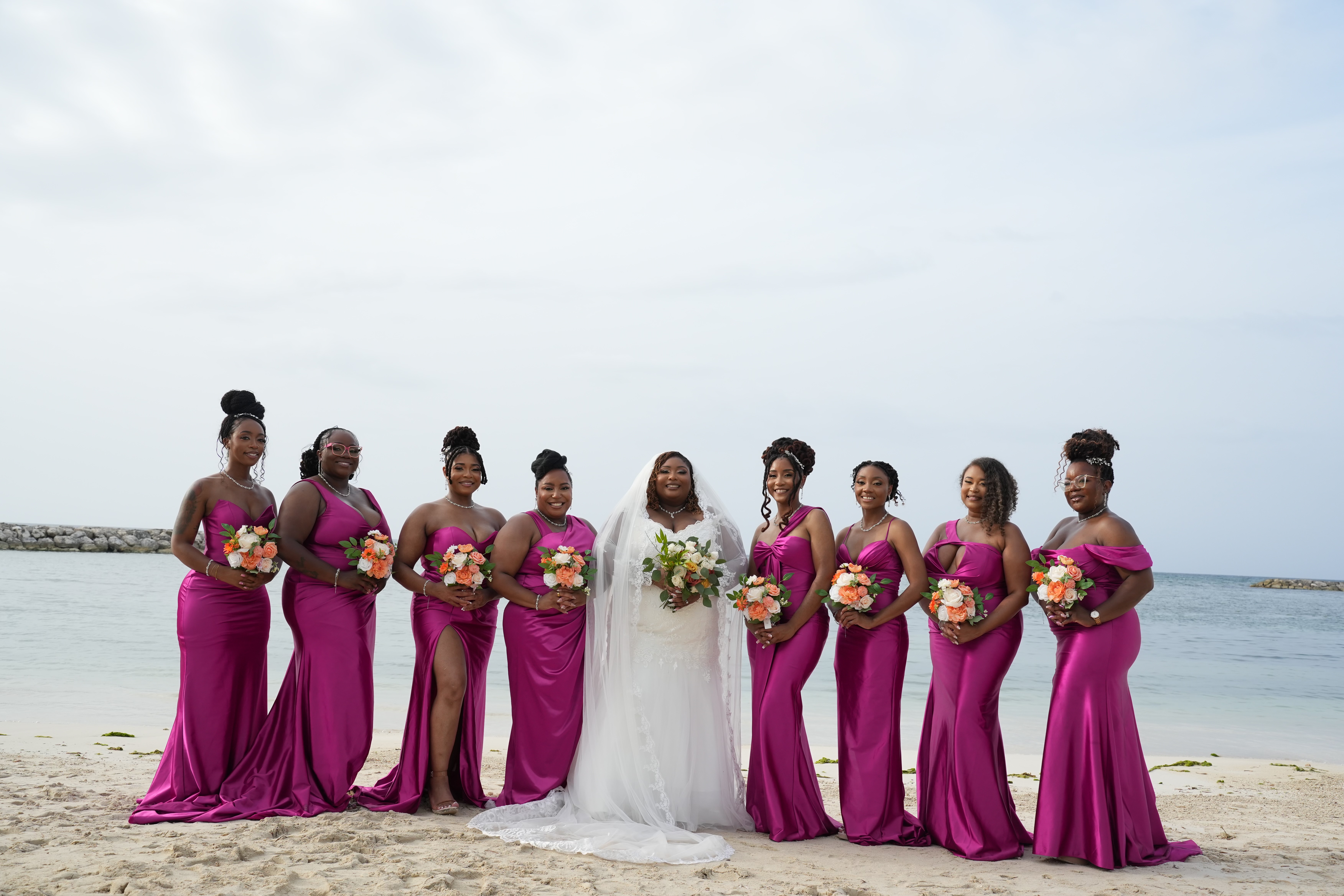 Kiah and Rodney's destination wedding: The bride in a white gown stands on the beach with her bridesmaids dressed in magenta.