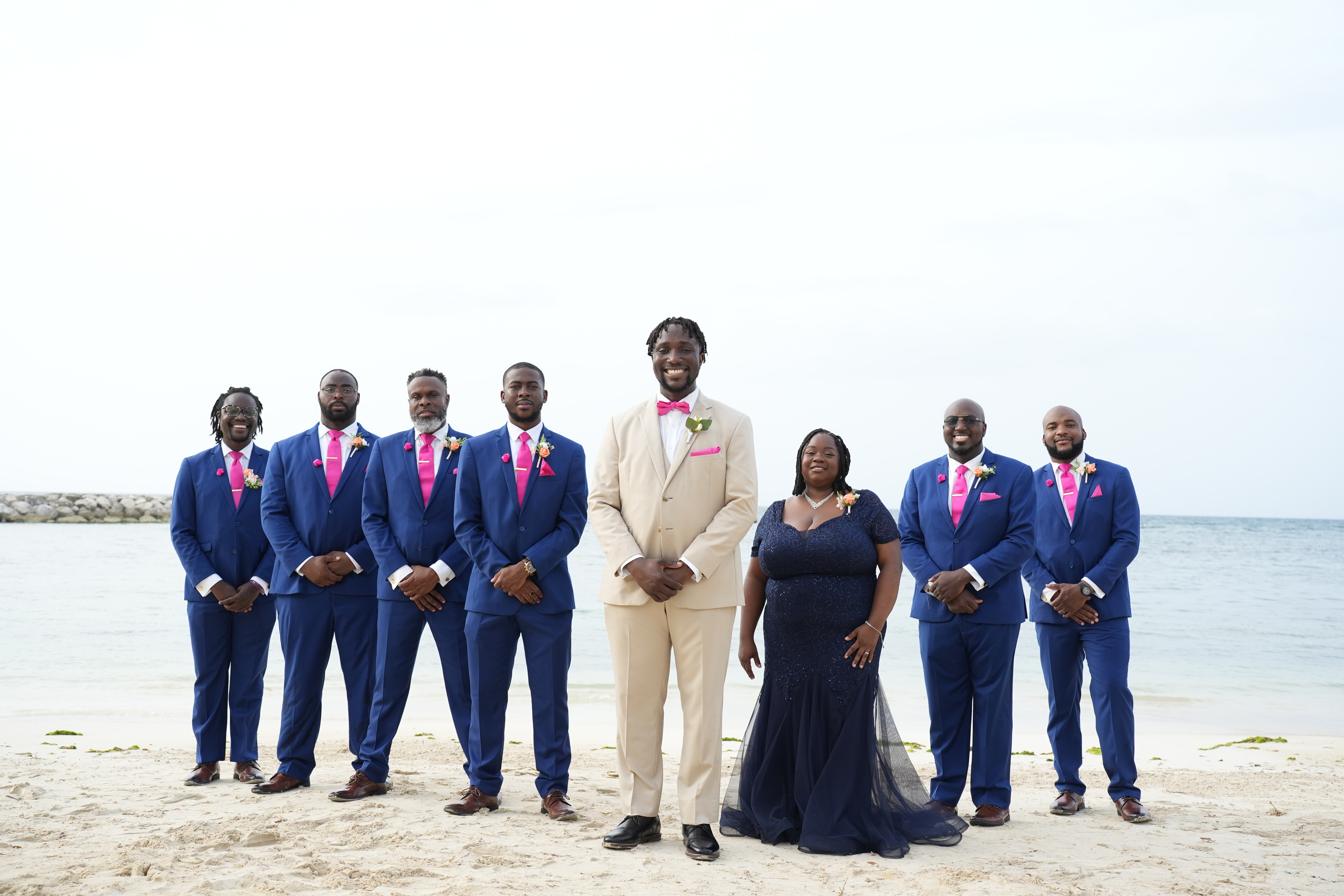 Kiah and Rodney (Copy): A destination wedding party gathers on a beach, with the ocean and sky creating a stunning backdrop behind them.