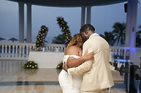 Kiah and Rodney share a close dance outdoors at their destination wedding, elegantly dressed and surrounded by beautiful floral decorations.