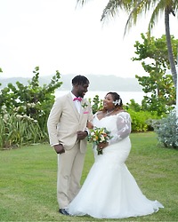 Kiah and Rodney smile together outdoors at their destination wedding, with lush greenery and shimmering water in the background.
