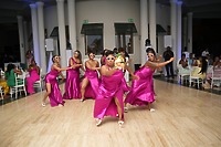 Six women in pink dresses and sunglasses dance at Kiah and Rodney’s destination wedding, entertaining seated guests.