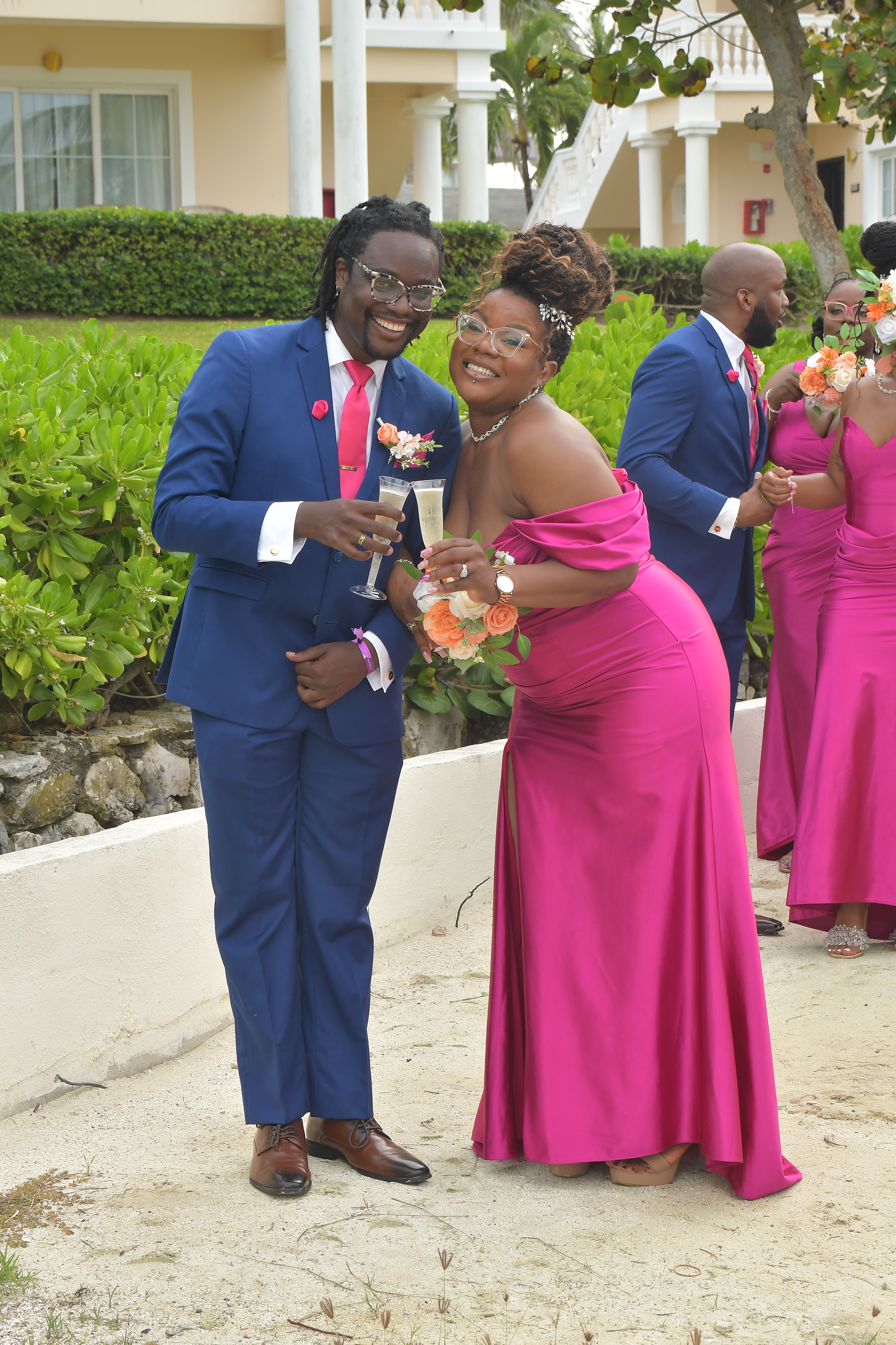 Kiah and Rodney, dressed in formal attire, smile while holding drinks at a destination wedding outdoor celebration.
