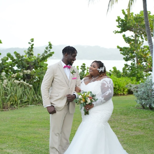 Kiah and Rodney smile together outdoors, surrounded by lush greenery, celebrating their destination wedding.