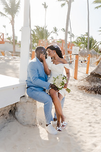 Mallory and Kharey, dressed for their destination wedding, sit close on the beach with a bouquet.