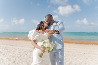 Mallory and Kharey share a kiss on the sand during their destination wedding, bouquet and waves behind.
