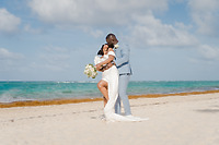 Mallory and Kharey (Copy) embrace on a sandy beach during their destination wedding by the ocean.