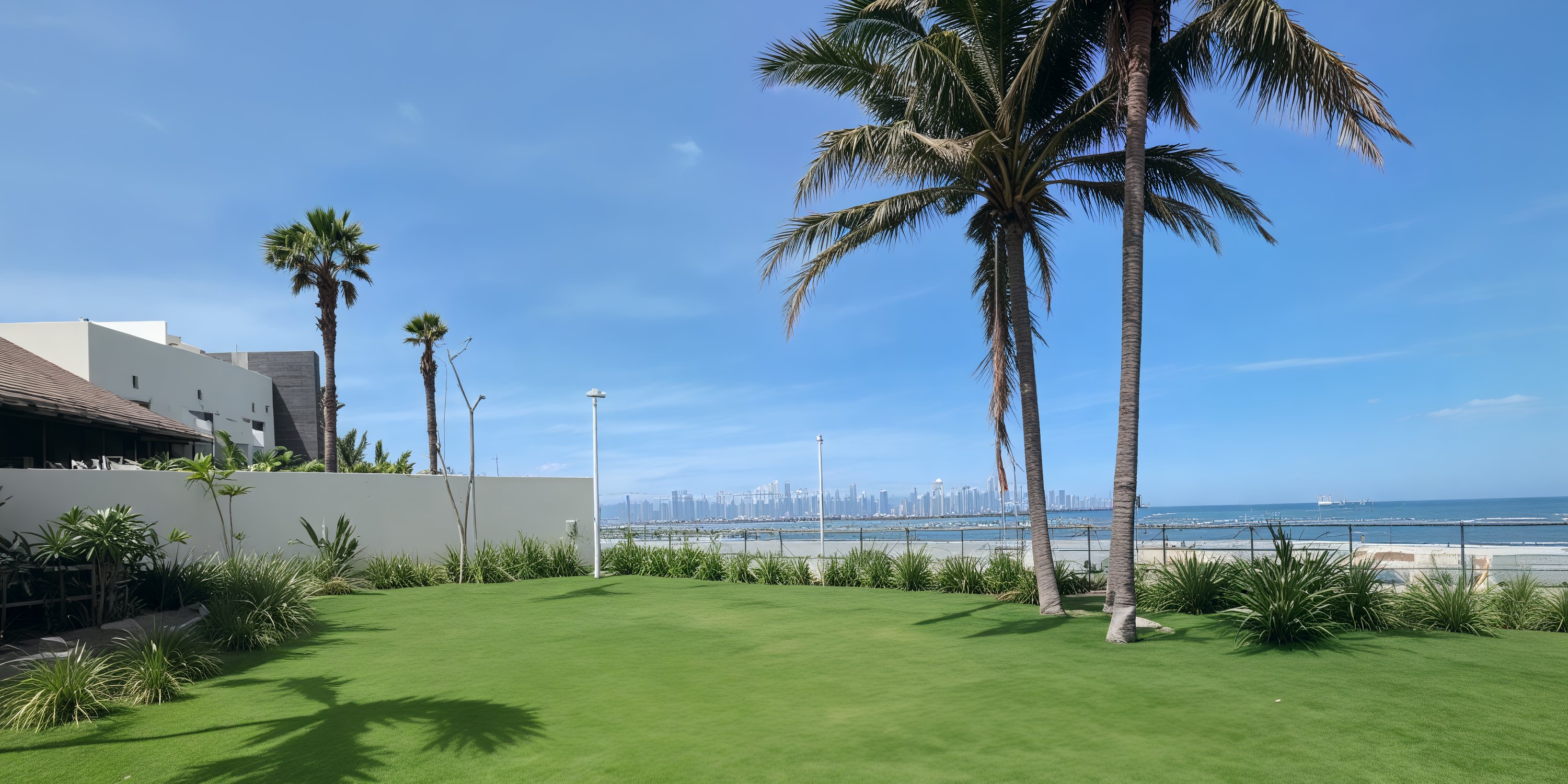 Green lawn with palm trees by the ocean, perfect for a destination wedding, city skyline in background.