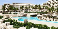 Modern resort ideal for a destination wedding, with pools, palm trees, lounge chairs, and white buildings.
