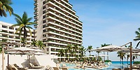 Tall modern hotel with balconies, perfect for a destination wedding, with poolside chairs and palm trees.