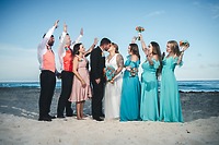 Mobolaji and Sylvia (Copy) kiss on the beach at their destination wedding as friends cheer around them.