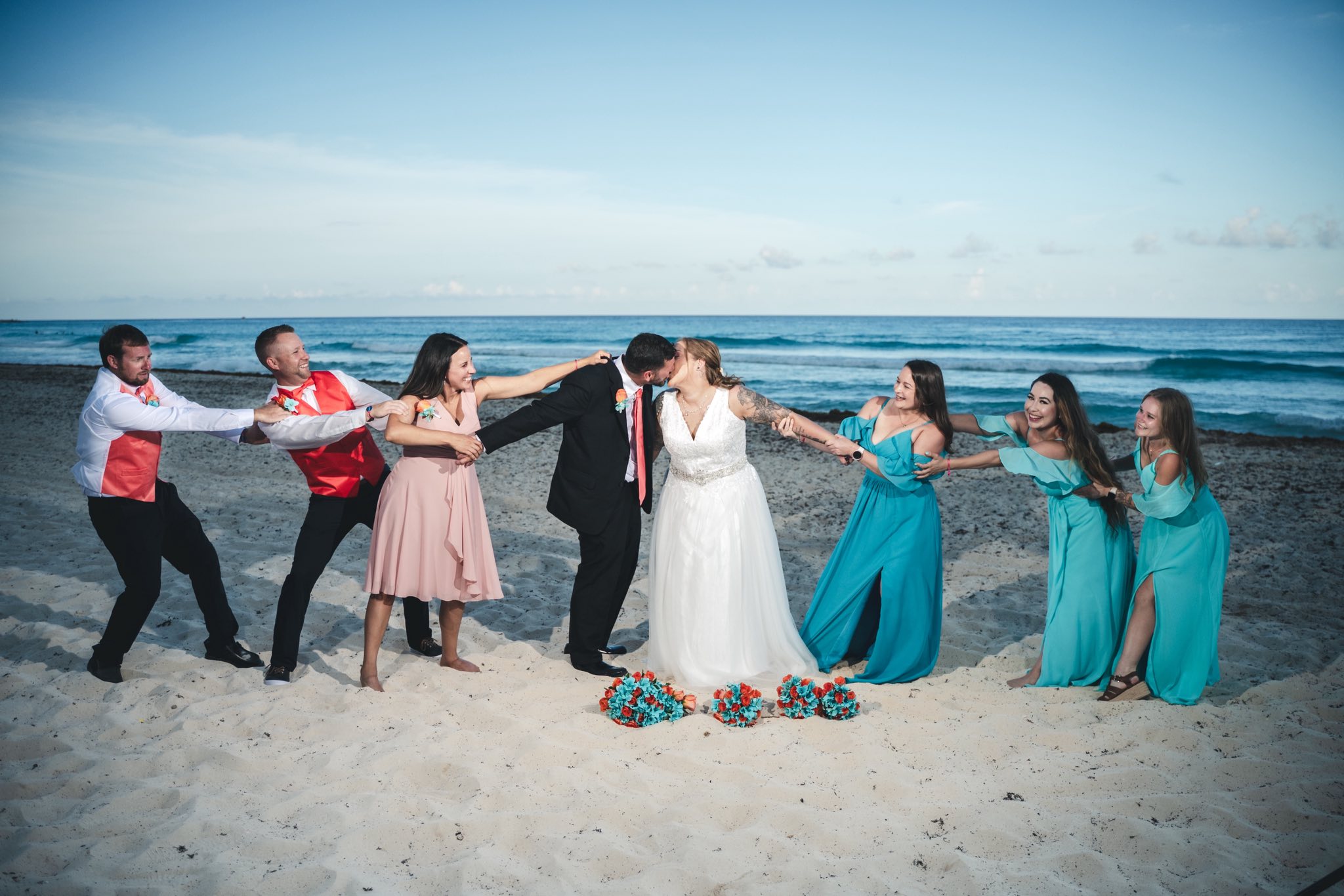 At their destination wedding, Mobolaji and Sylvia kiss on the beach as friends playfully pull them apart.