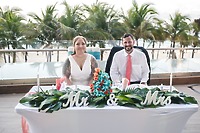 Mobolaji and Sylvia sit at a decorated table with "Mr & Mrs" sign at their destination wedding, palm trees behind.