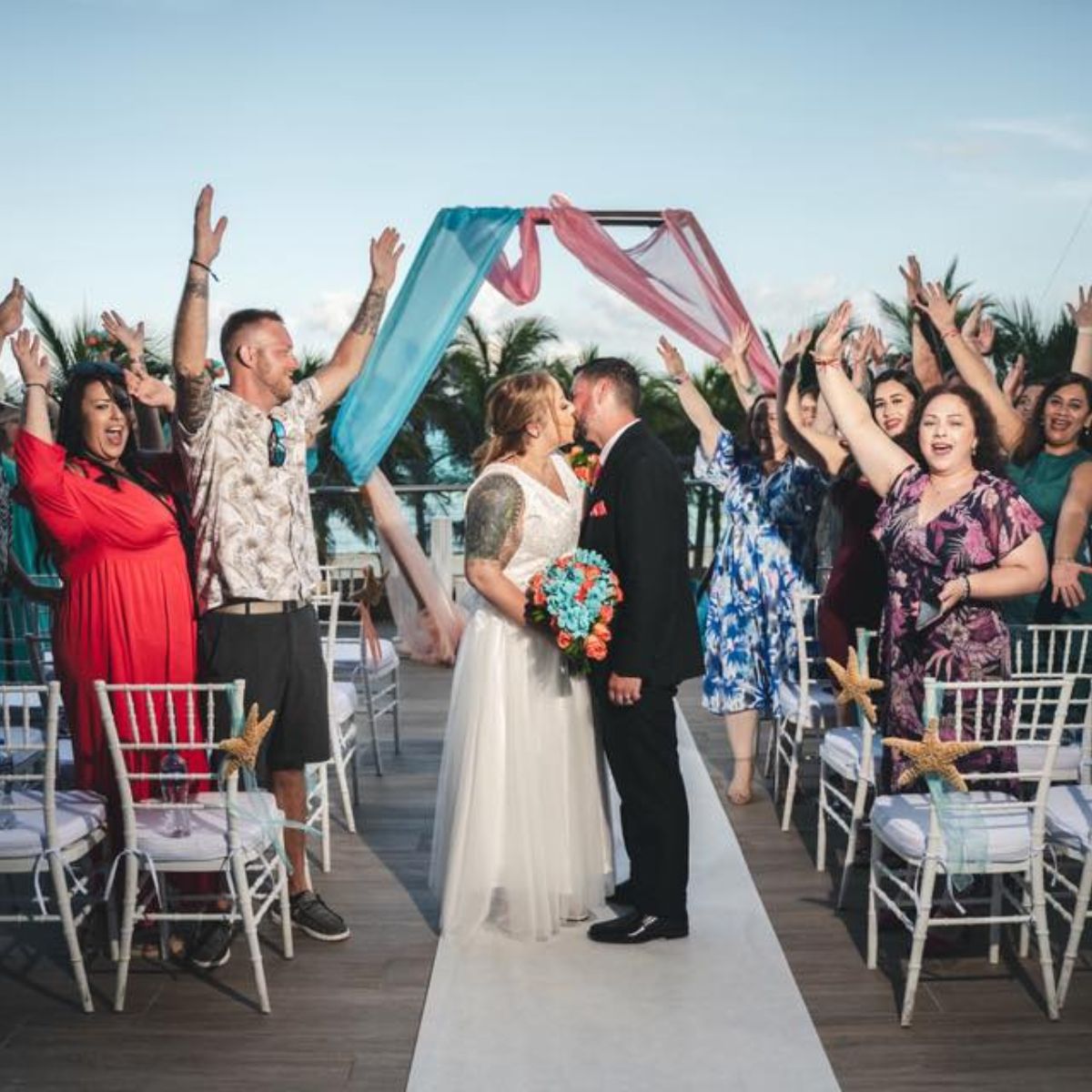 Mobolaji and Sylvia kiss at their destination wedding while guests cheer and raise their arms in celebration.