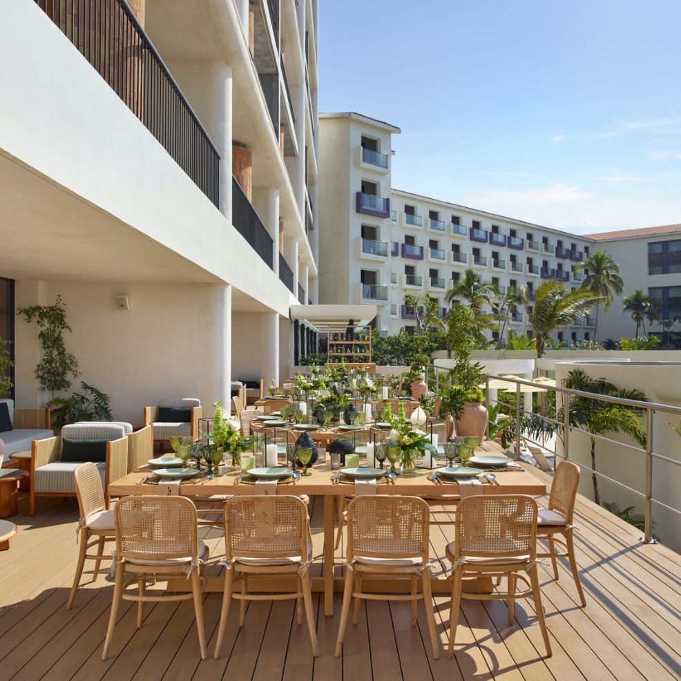 Outdoor dining table set for a destination wedding on a wooden patio at a modern resort with palm trees.