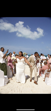 Jordan and Kievan walk down the aisle at their destination wedding on a sandy beach, surrounded by their guests.