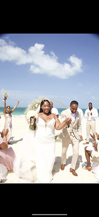 Jordan and Kievan stroll along the beach, celebrating their destination wedding with their bridal party under clear blue skies.