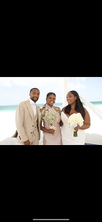Three people dressed in formalwear stand on a beach, each holding bouquets—capturing the essence of a destination wedding.