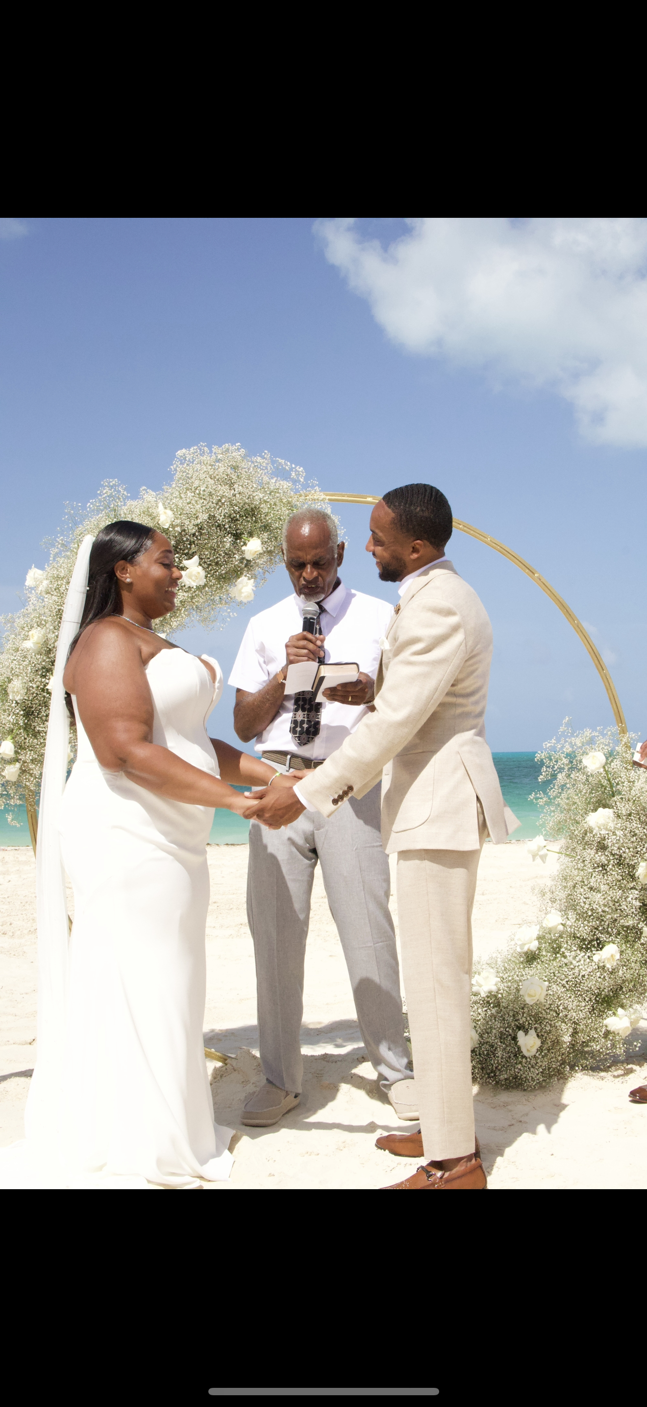 Jordan and Kievan’s destination wedding takes place on a beach, where the couple exchanges vows beneath a floral arch with an officiant guiding the ceremony.