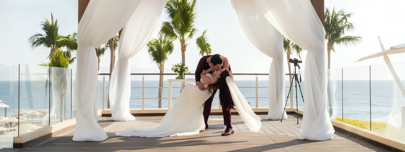 The bride and groom share a romantic kiss beneath a canopy at their beautiful destination wedding by the sea.