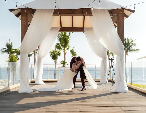 The bride and groom share a kiss beneath a white canopy at their beautiful oceanfront destination wedding.