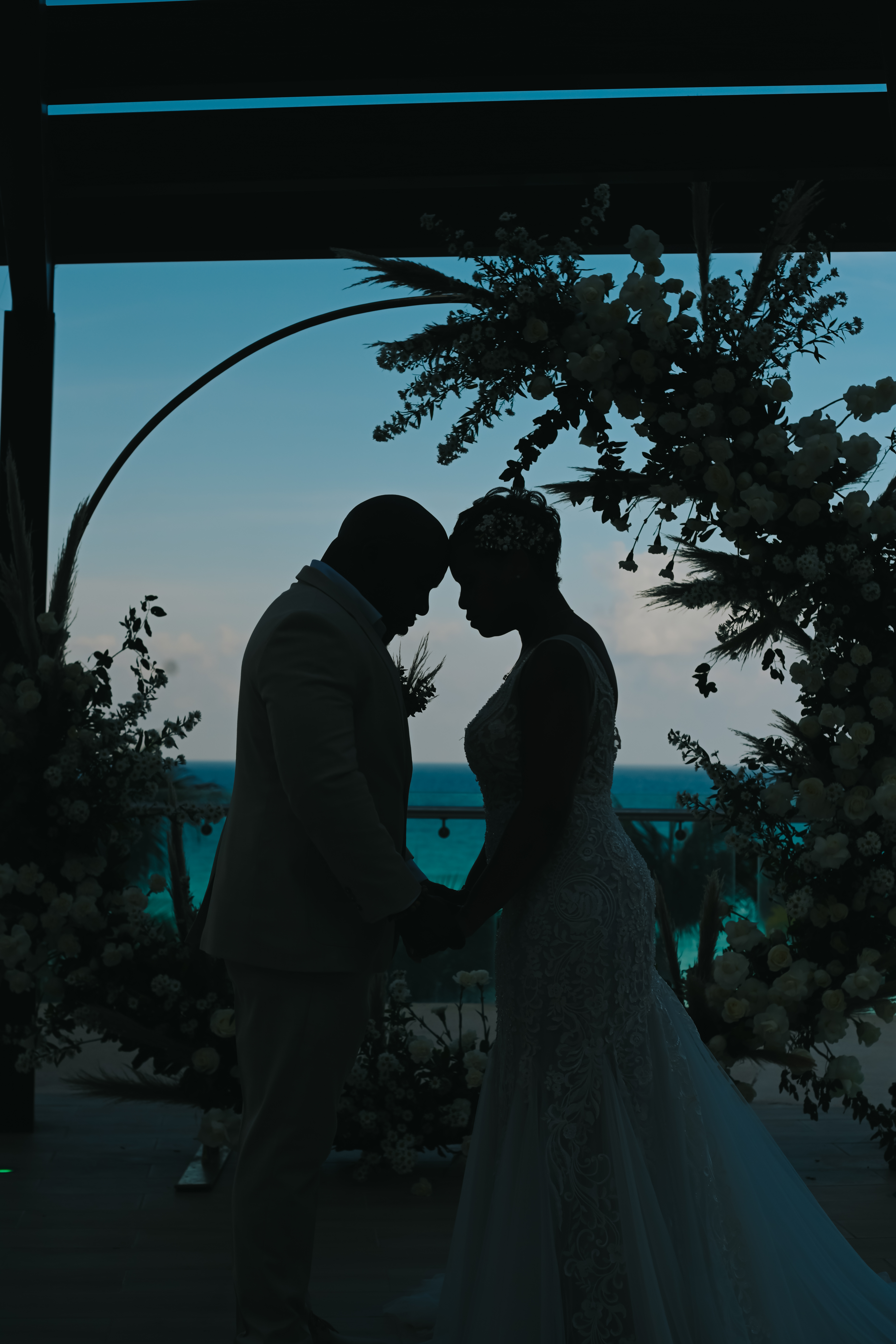 April and Javiert holding hands under a floral arch at their destination wedding by the ocean.