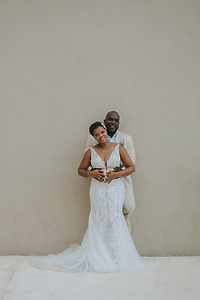April and Javiert (Copy) smile in wedding attire, posing for a destination wedding against a beige wall.