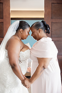 April and Javiert stand forehead to forehead, holding hands in a sunlit destination wedding room.