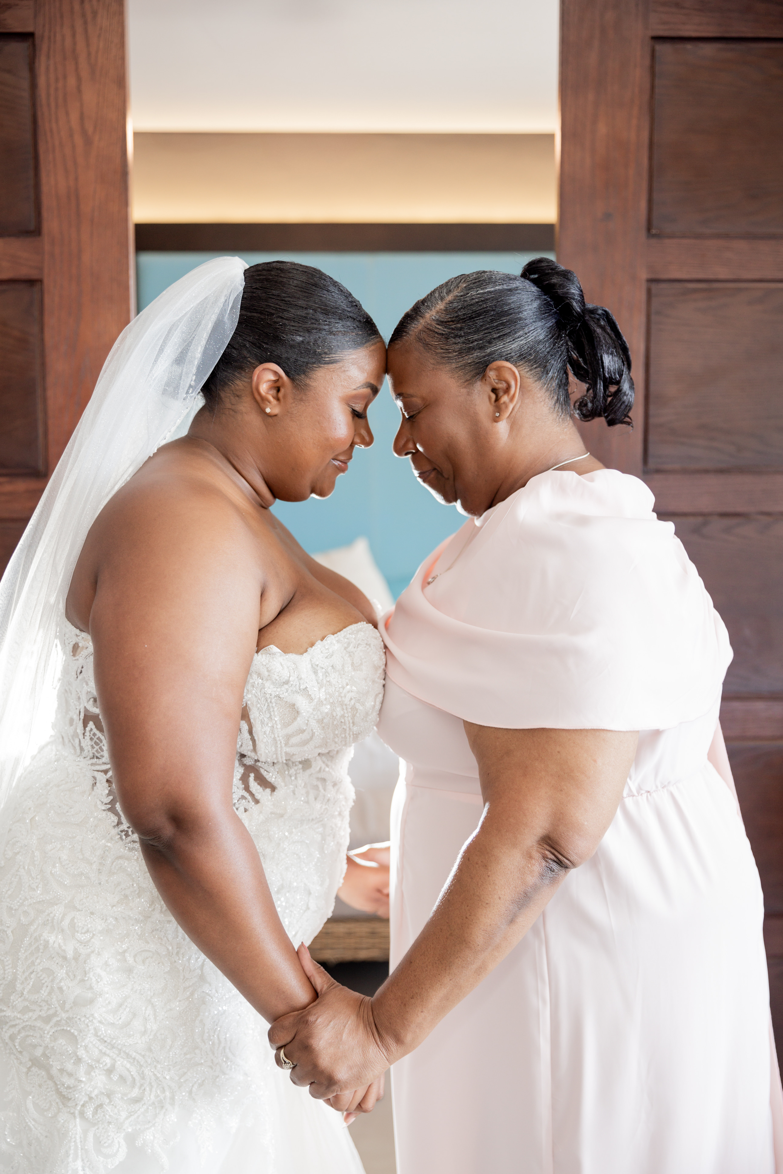 April and Javiert stand forehead to forehead, holding hands in a sunlit destination wedding room.