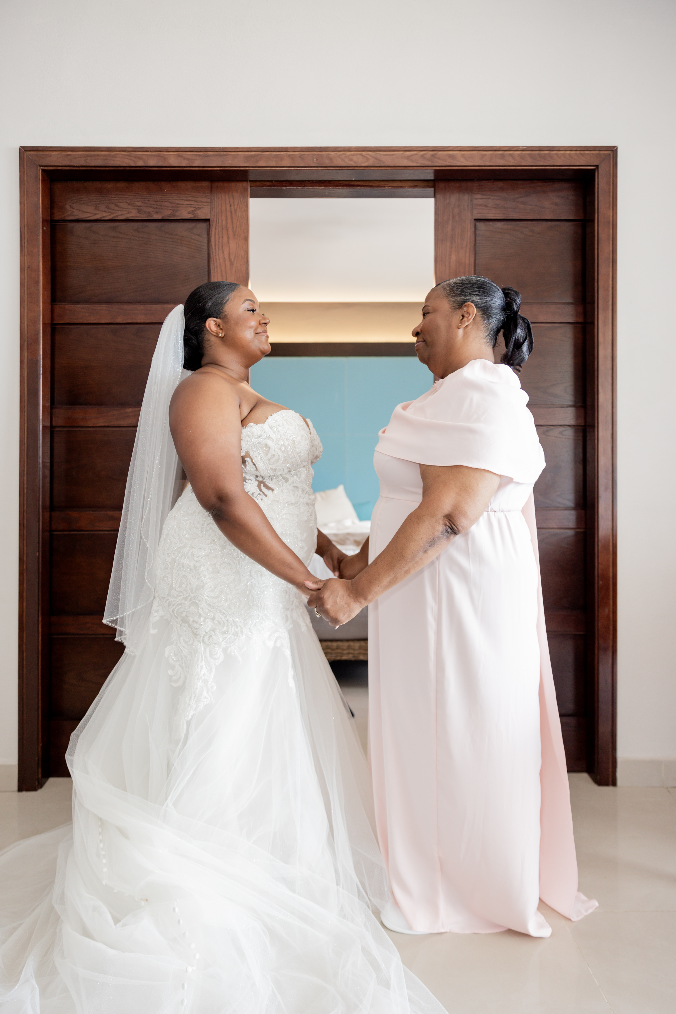 April and Javiert: At a destination wedding, the bride in white holds hands with a woman in light pink.