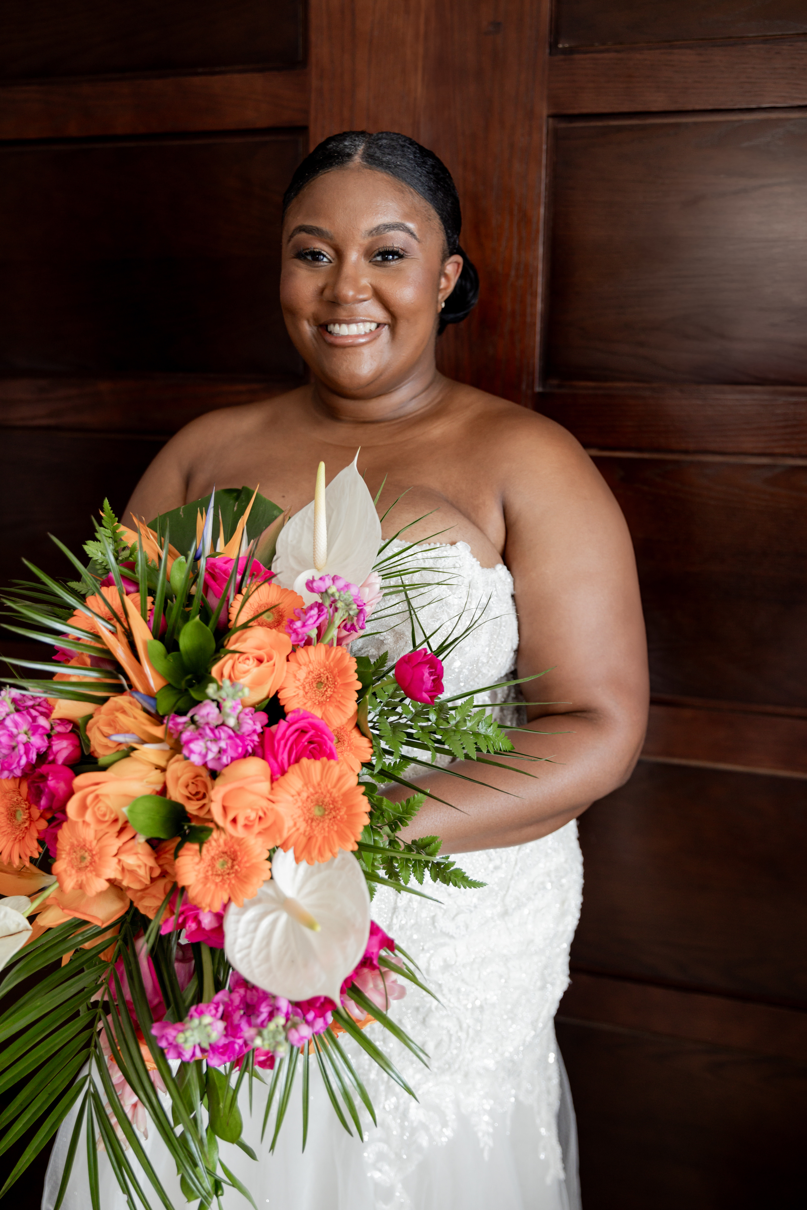 Bride in an April and Javiert dress holds a vibrant bouquet before wooden panels at a destination wedding.
