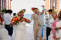 Jessie and Taylor celebrate as they walk down the aisle, smiling at their destination wedding on the beach.