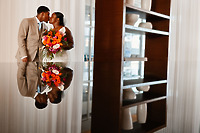 Jessie and Taylor smile indoors at their destination wedding, a vibrant bouquet reflected on a glossy surface.