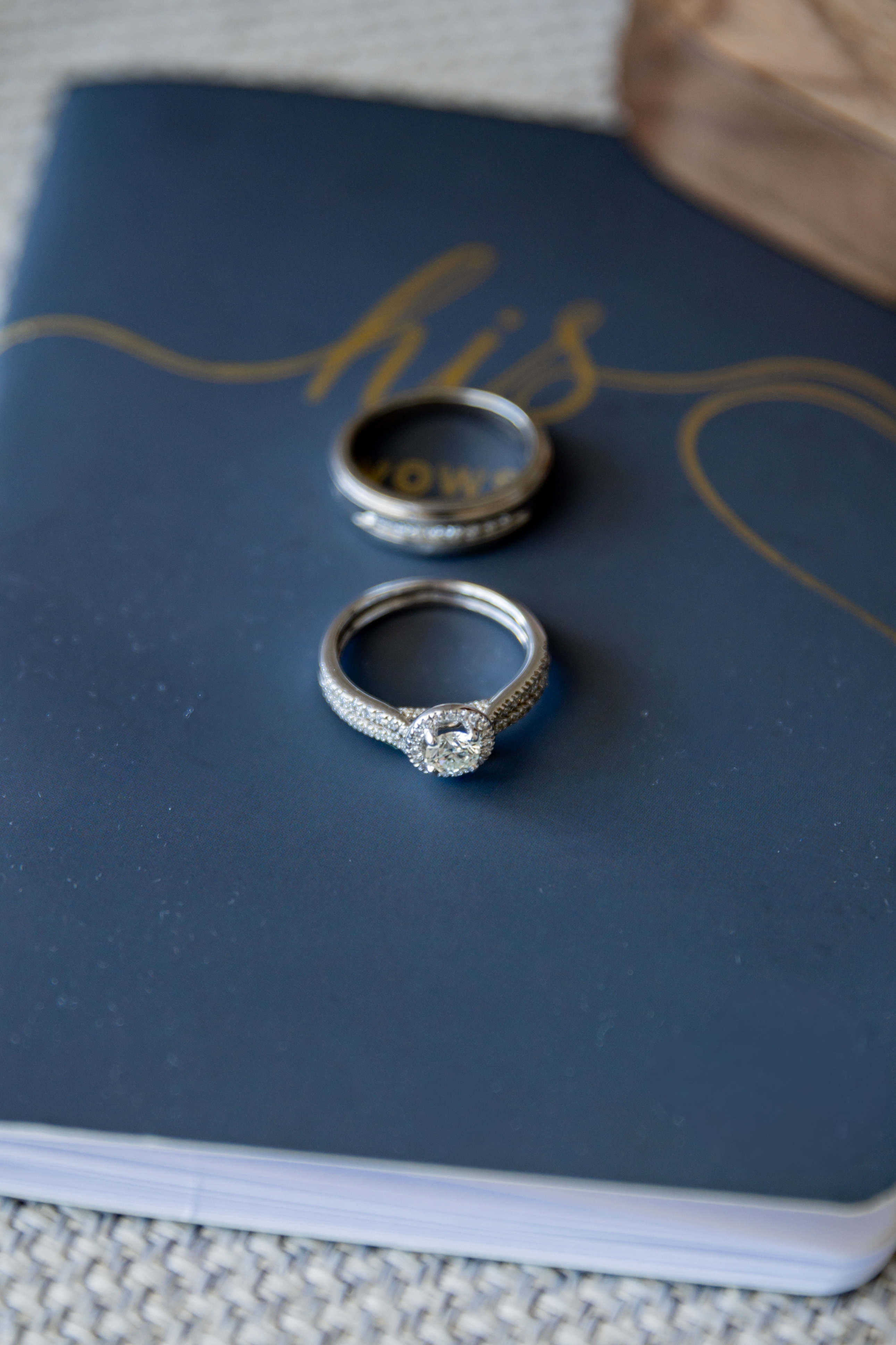 April and Javiert's wedding rings sit atop a dark blue "his vows" book with elegant gold lettering.
