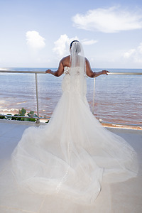 Bride in an April and Javiert dress stands on a balcony overlooking the ocean at a destination wedding.