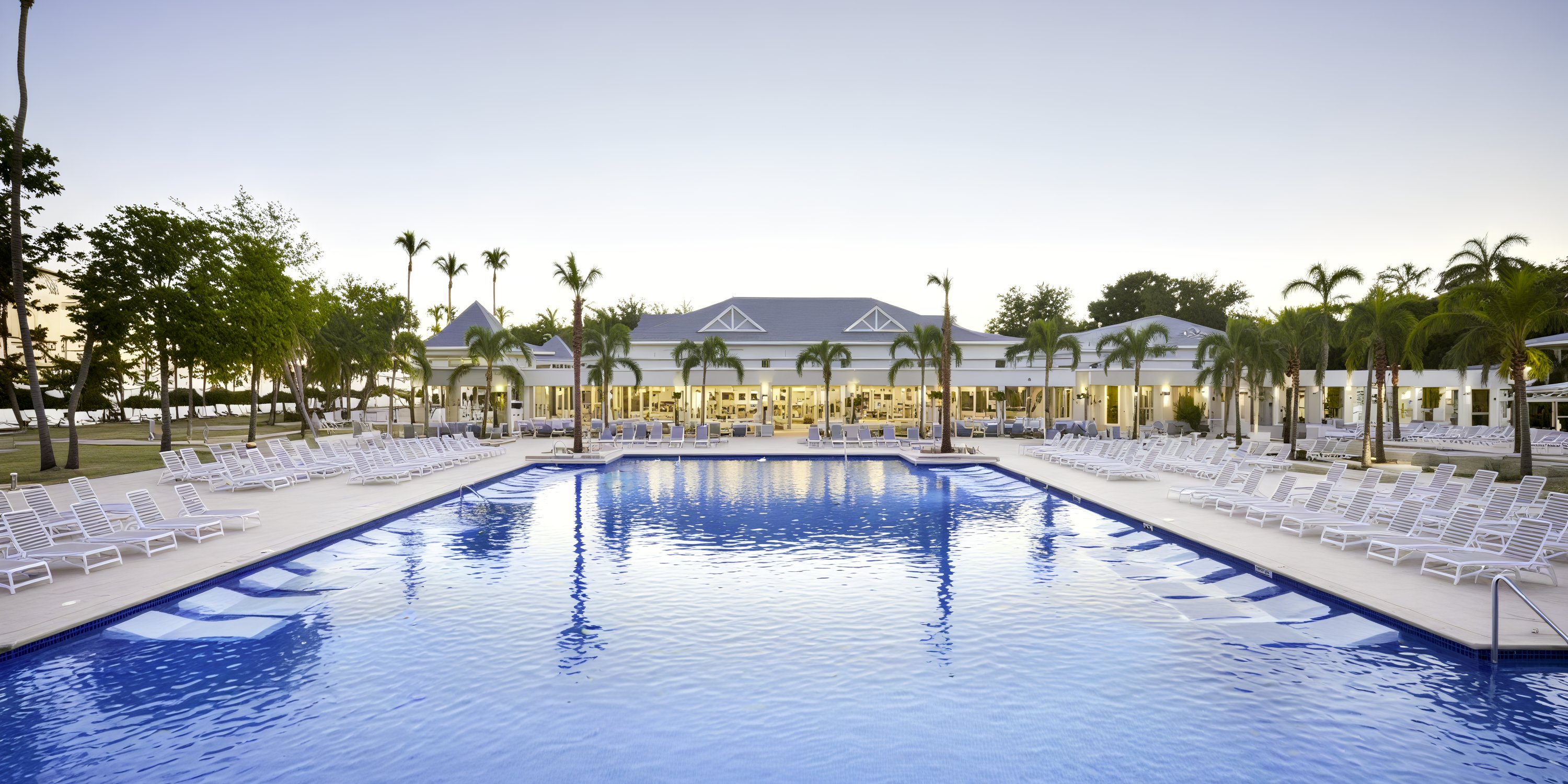 Large outdoor pool with white lounge chairs and palm trees, ideal for a destination wedding at Bahia Principe Grand Samana.