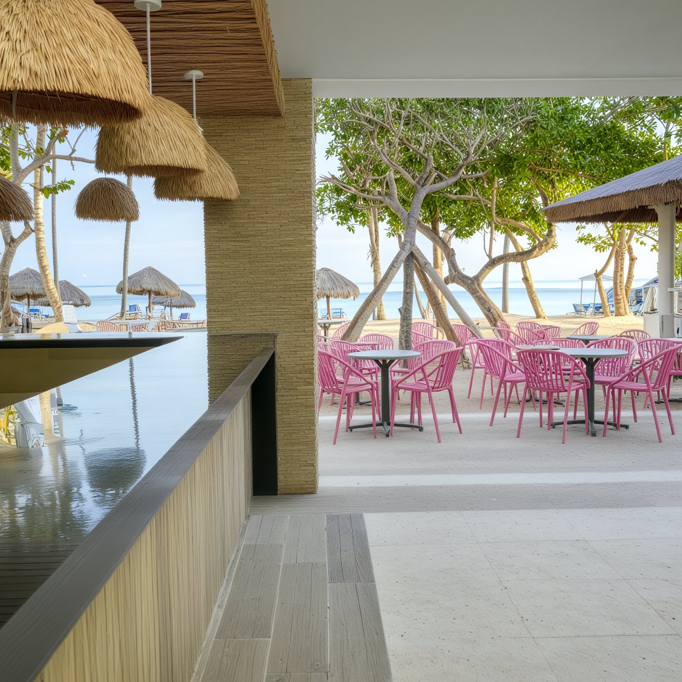 Chic outdoor patio with pink chairs and tables, perfect for a destination wedding, near the beach bar.