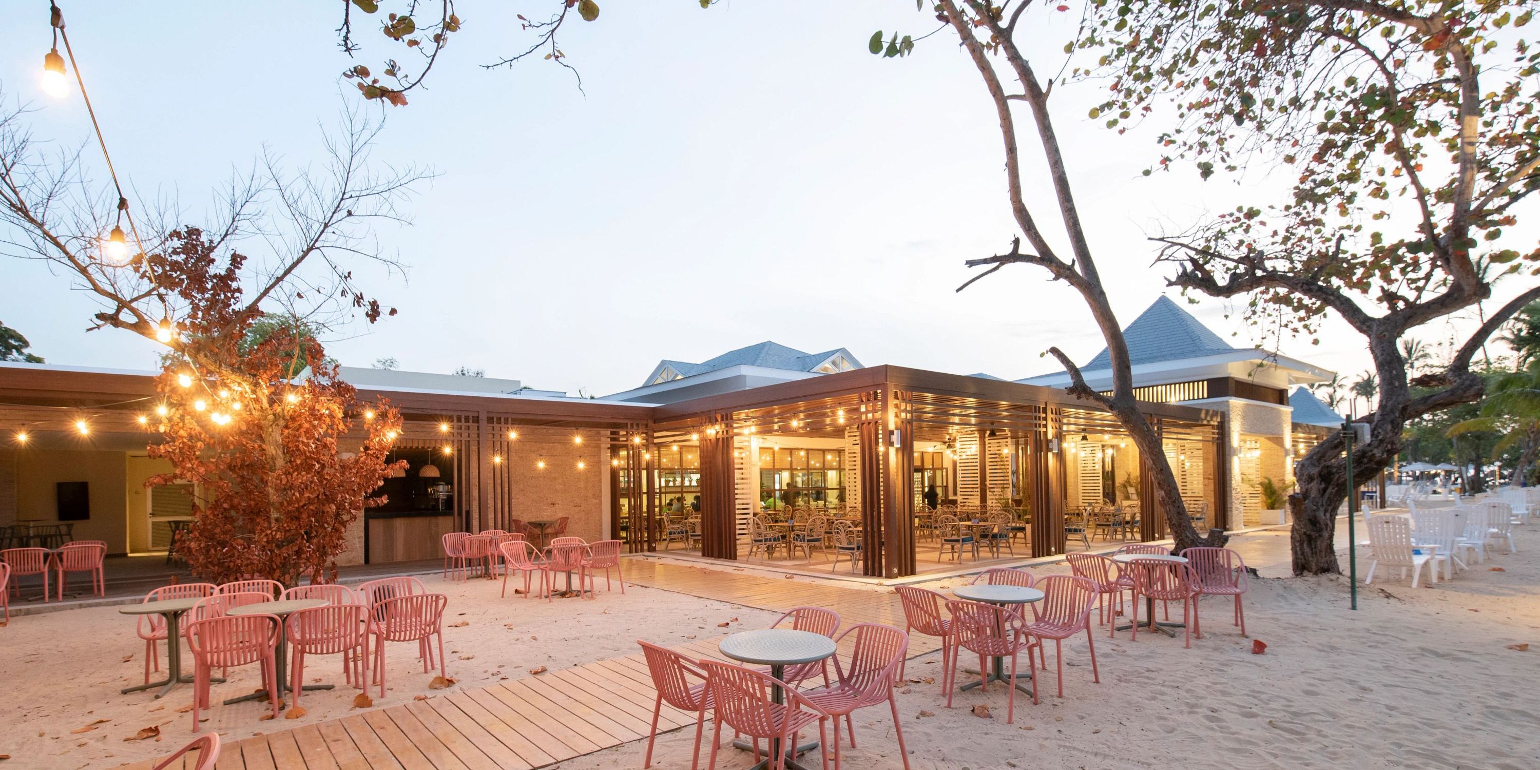 Bahia Principe Grand El Portillo&rsquo;s beachside restaurant set for a destination wedding at sunset, with pink chairs and string lights.