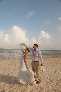 April and Javiert dance in wedding attire on a sandy beach, enjoying their destination wedding by the ocean.